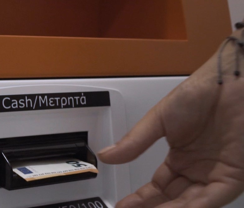 Photo of a hand inserting paper cash bills into a Bitcoin ATM